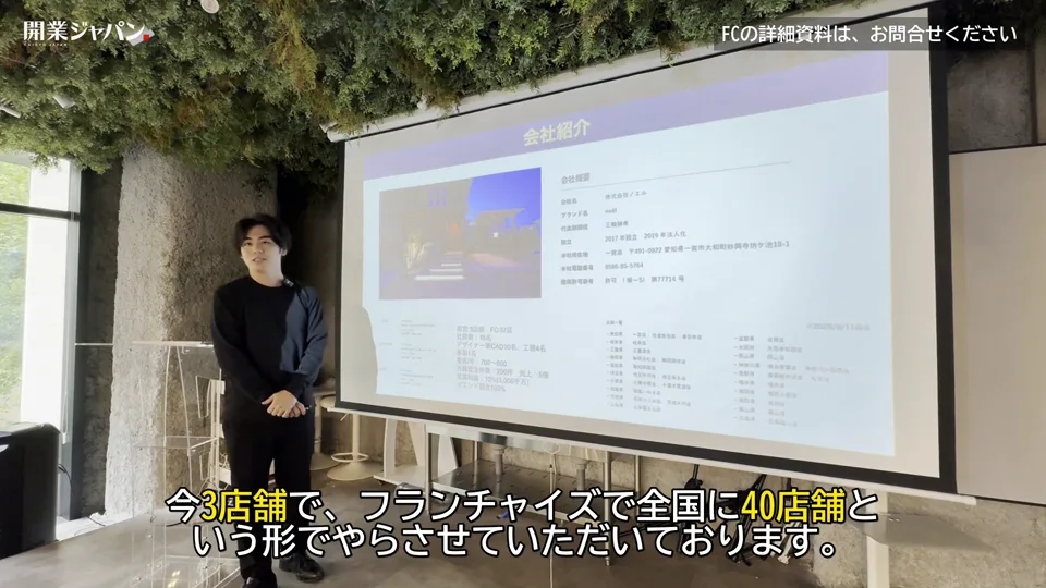 会社紹介スライドの前で直営3店舗・FC40店舗と説明する三輪社長